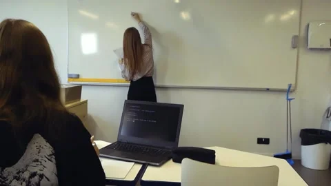 Teacher writing on a whiteboard while student watches with a laptop Stock Footage 344860177