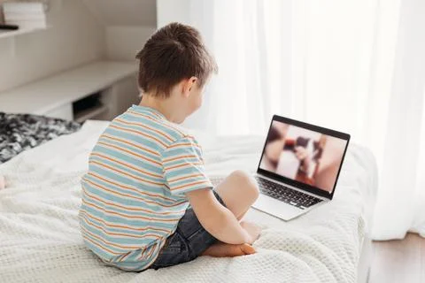 Teaching children at home using the Internet. The boy is sitting on the bed and Stock Photos