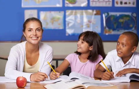 Teaching is very rewarding. A young teacher sitting with her two ethnic pupils Stock Photos