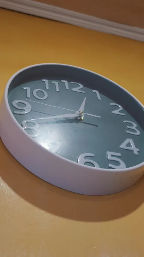 Teal Analog Wall Clock with White Hands Mounted on a Bright Yellow Interior Wall Video stock 333825904