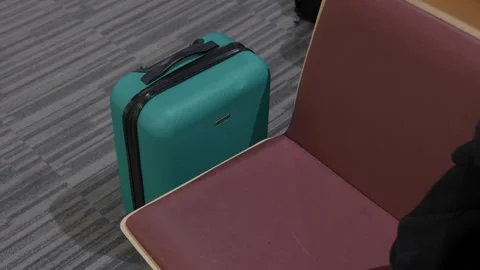 Teal hard shell suitcase beside seat at airport terminal waiting area Stock Footage 337913116