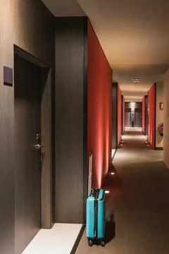 A teal hardshell suitcase stands in a modern hotel corridor beside an open .. Stock Photos
