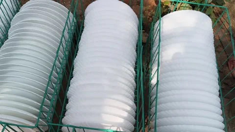 A teal wire basket filled with several white, scalloped-edge plates. 库存影片 329217617