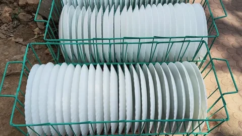 A teal wire basket filled with several white, scalloped-edge plates. 库存影片 329217618