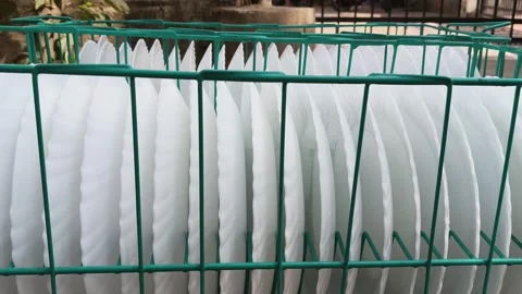 A teal wire basket filled with several white, scalloped-edge plates. 库存影片 329217623