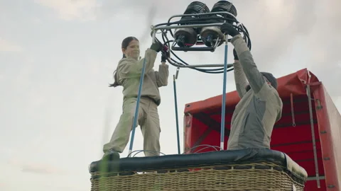 Team assembling hot air balloon burner onto basket in open field setup Stock Footage 317188135