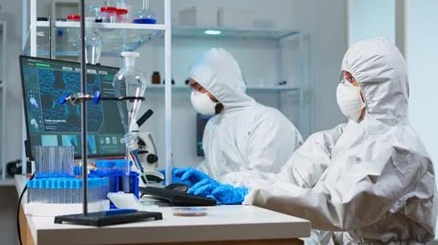 Team of biologists in coverall working with microscope and computer Stock Photos
