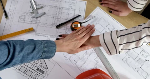 A team of builders architects stands over a table with blueprints holding hands  Stock Footage 201692709