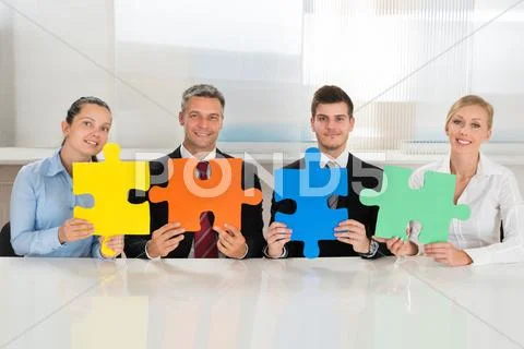 Team Of Businesspeople Holding Four Multi-colored Puzzles At Desk Stock Photos