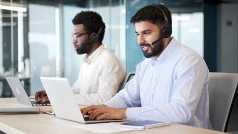 Team of call center agents wearing headsets working on laptops in office. Vídeo Stock 329052386