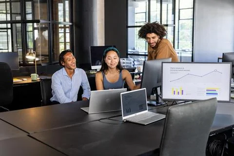 Team collaborating in modern office, analyzing graphs on laptops and monitor Foto stock