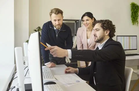 Team of colleagues discussing project data at computer in office strategy Stock Photos