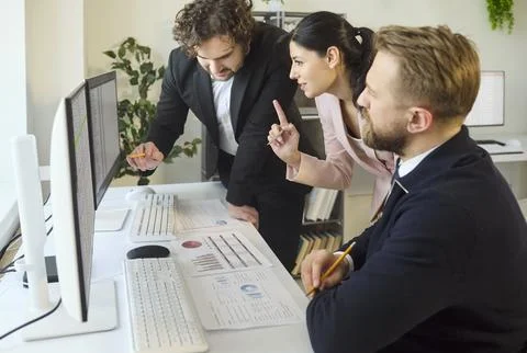 Team of coworkers analyzing charts on computer screens during office meeting Stock Photos