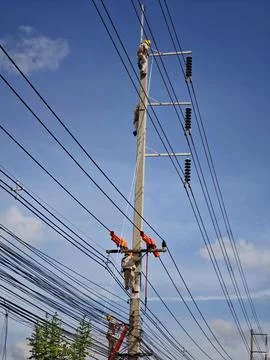 Team of electrical lineman workers climbing concrete pole with safety. Stock Photos