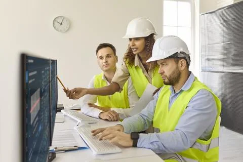Team of engineers analyzing production data on screens in modern control room Stock Photos