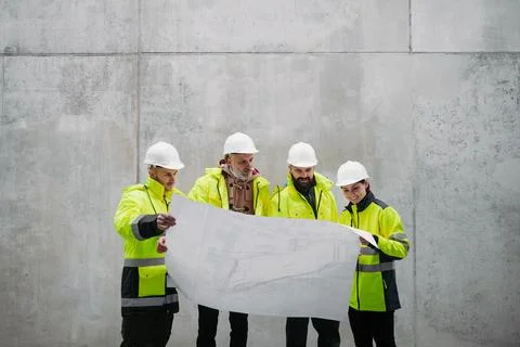 Team of engineers and construction workers reviewing blueprints, building site. Fotos de archivo