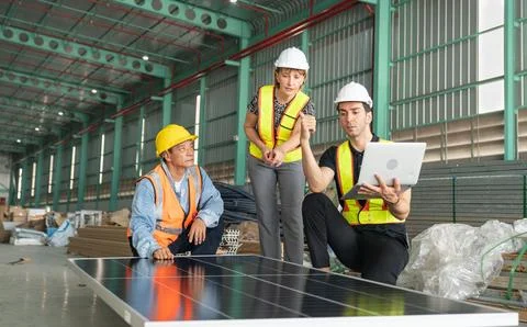 Team of engineers and technicians working on solar panel in large warehouse Foto stock