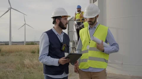 Team engineers men discuss maintenance of windmill in safety clothing using Stock Footage 256092046
