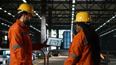 Team of engineers oversee robotics software on laptop in heavy industry workshop Stockfoto's