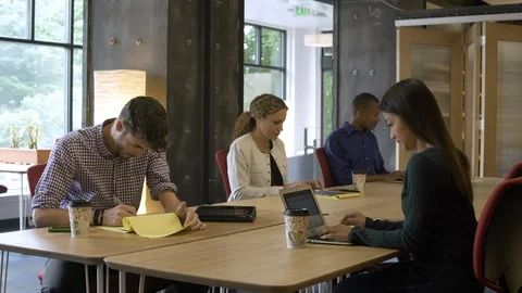 Team of four sitting and working at table, typing on digital devices and Stock Footage 88027349