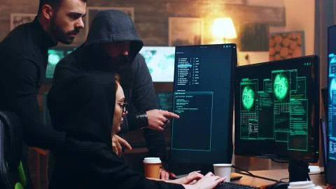 Team of hackers looking at computer with multiple monitors Stockfoto's