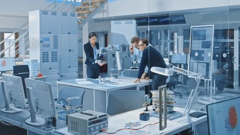Team of Industrial Robotics Engineers Gathered Around Table With Robot Arm Stock Footage 105355550