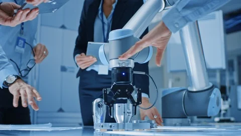 Team of Industrial Robotics Engineers Gathered Around Table With Robot Arm Stock Footage