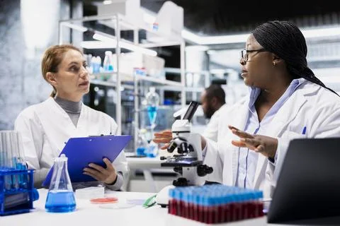 Team of lab experts checking product surface for tiny defects using microscope Stock Photos
