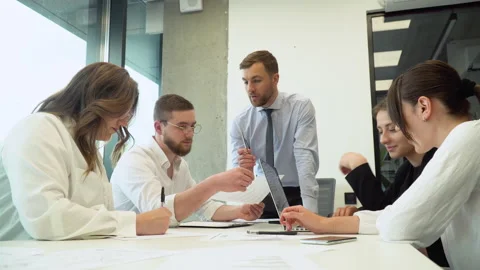 Team leader sitting at table with colleagues, discussing working issues at Stock Footage 196260619