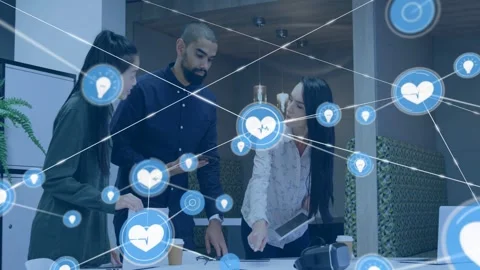 Team leaning around table, right pointing tablet spawning heart-pin icon web Stock Footage 333004777