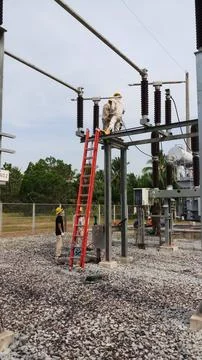 Team of lineman electrician workers using red extension ladder performing . Stock Photos