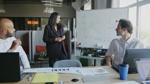 A team meets in an office to discuss project updates. The presenter explains Vídeos de archivo 335731519