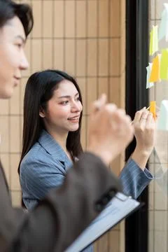 Team members collaborating on project ideas with sticky notes on a glass board. Stock Photos