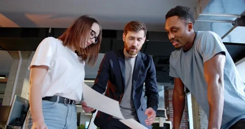 Team of mixed-races men and woman standing over the table and discussing project Stock Footage 180072691