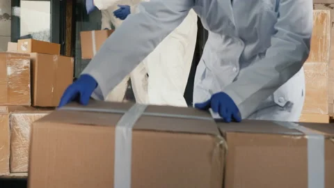 A team of movers loads boxes into the car. All in protective antiviral suits Stock Footage 131250899