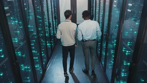 Team of multi-race IT engineers walking in server rack corridor discussing work Stock Footage 119232753