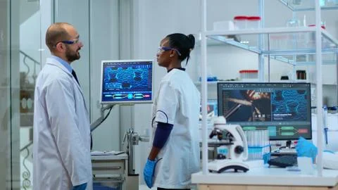 Team of multiethnic scientists analysing test trial vaccine using computer Stock Photos