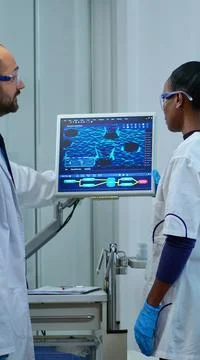 Team of multiethnic scientists analysing test trial vaccine using computer Stock Photos