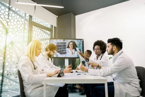 Team of multiracial five doctors sitting in light office, having video 스톡 사진