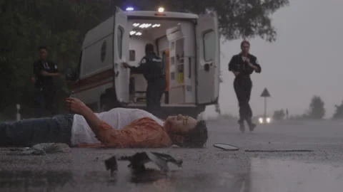 Team of paramedics helping man lying on road under rain Stock Footage 163881176