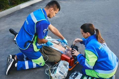 Team of paramedics performing CPR with mobile defibrillator and preparing man Stock Photos