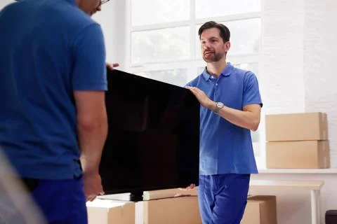 Team Of Pro Movers Delivering Large TV Into New Home. Stock Photos