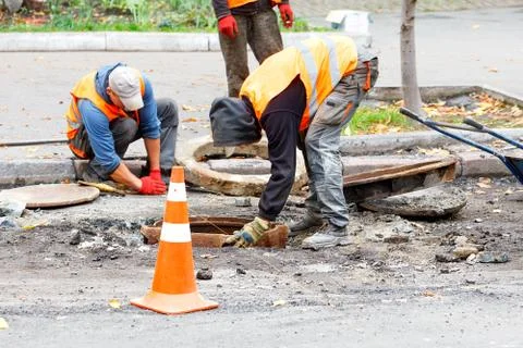 A team of road workers are replacing the old sewerage manhole with a new one. Stock Photos