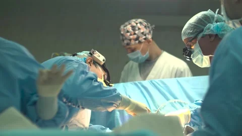 A team of surgeons bent over the operating table, performing a surgical Stock Footage 303650753