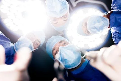 Team of surgeons operating under surgery lights Stock Photos