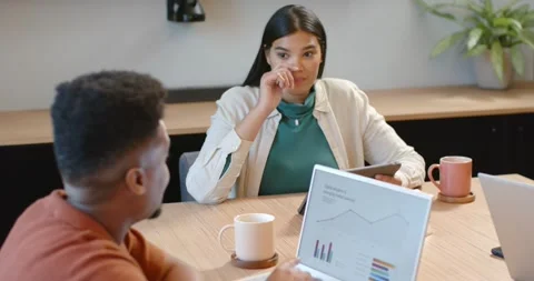 Team at table reviewing data, man in rust top raising laptop showing charts, Stock Footage 344964041