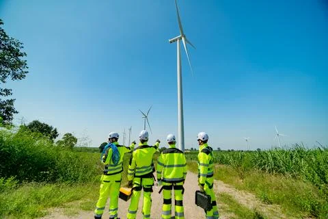 Team of technicians inspecting wind turbines in a green energy field during.. Stock Photos