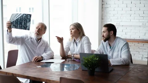 Team of three doctors discuss X-ray of patient in consulting room of hospital Stock Footage 125015495