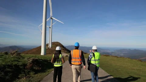 Team of three multicultural engineers walking and discussing near wind turbin Stock Footage 294976051
