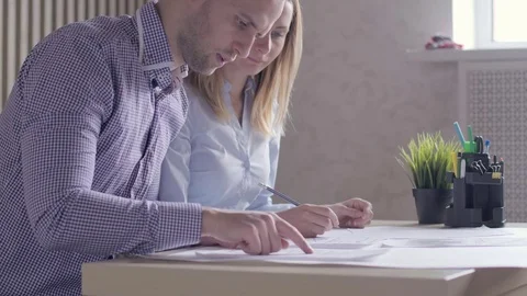 Team of two architects, sitting at desk in office with building plans Stock Footage 72985407